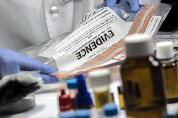 Photo of latex gloved hands holding sealed evidence bag.