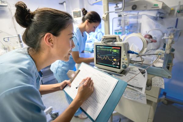 Photo of nurse reviewing hospital monitor for newborn baby.