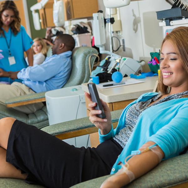 Photo of several people donating plasma. Woman smiling while looking at smartphone.